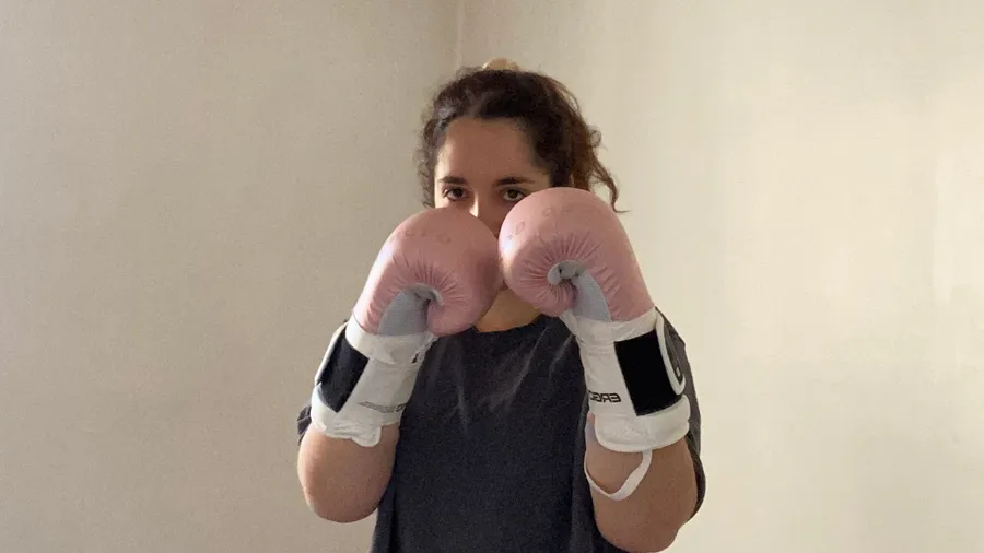 Pink boxing gloves up, eyes peeking over, bare white wall