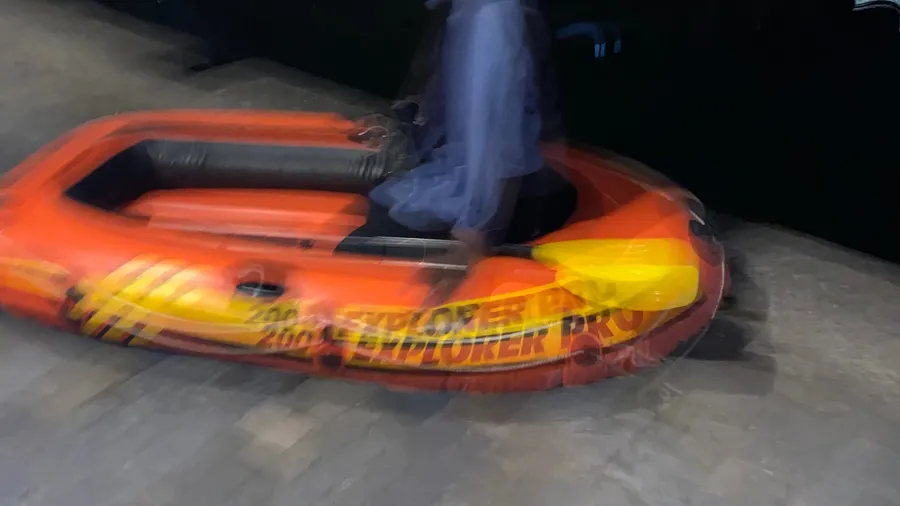 Orange inflatable dinghy streaking through the dark, someone standing in it