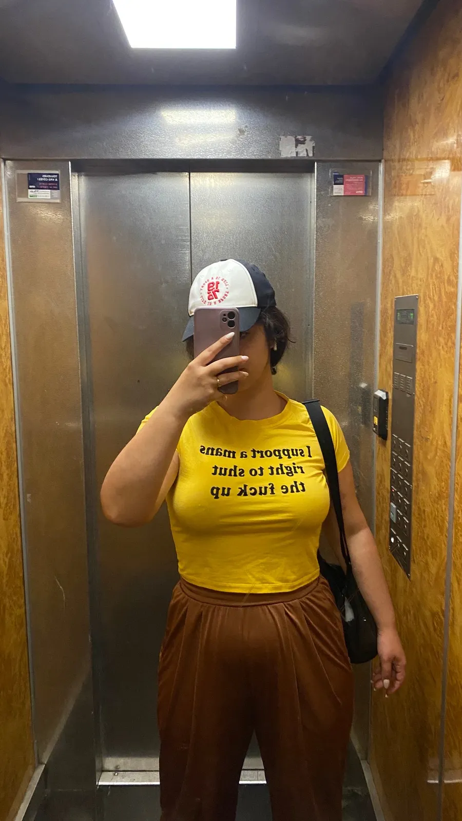 Lift mirror selfie, yellow slogan tee and brown trousers