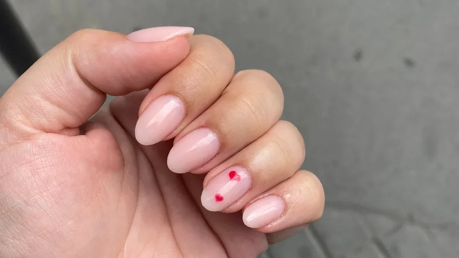 Pale pink nails, one with a tiny red heart