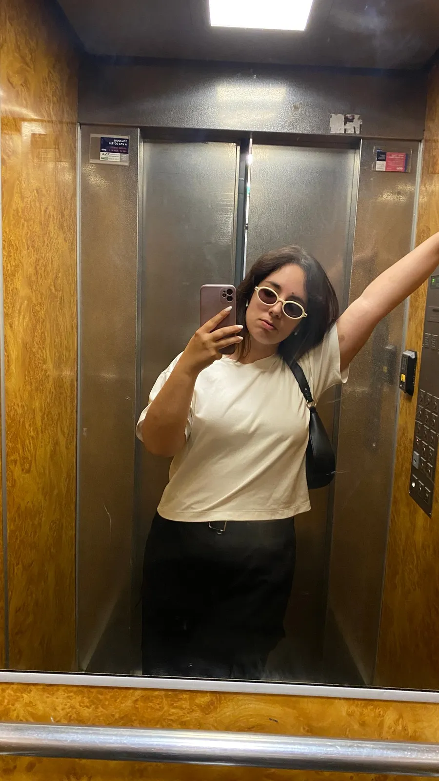 Lift mirror selfie, white sunglasses, arm up against the gold panelling