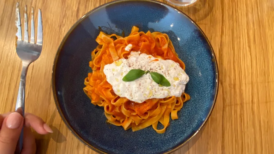 Tomato tagliatelle with burrata and basil, fork in hand