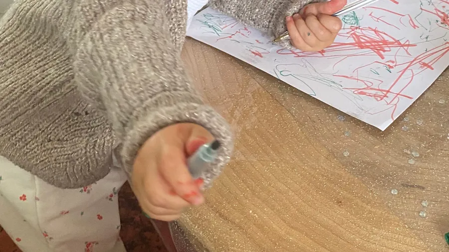 Small hand holding a marker over red scribbles