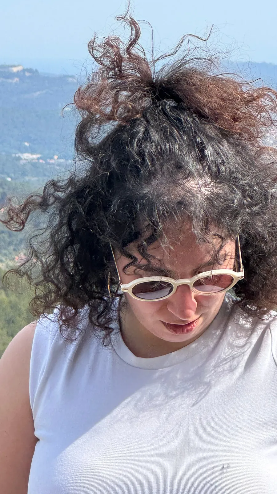 Wind-blown curls and white sunglasses, valley below