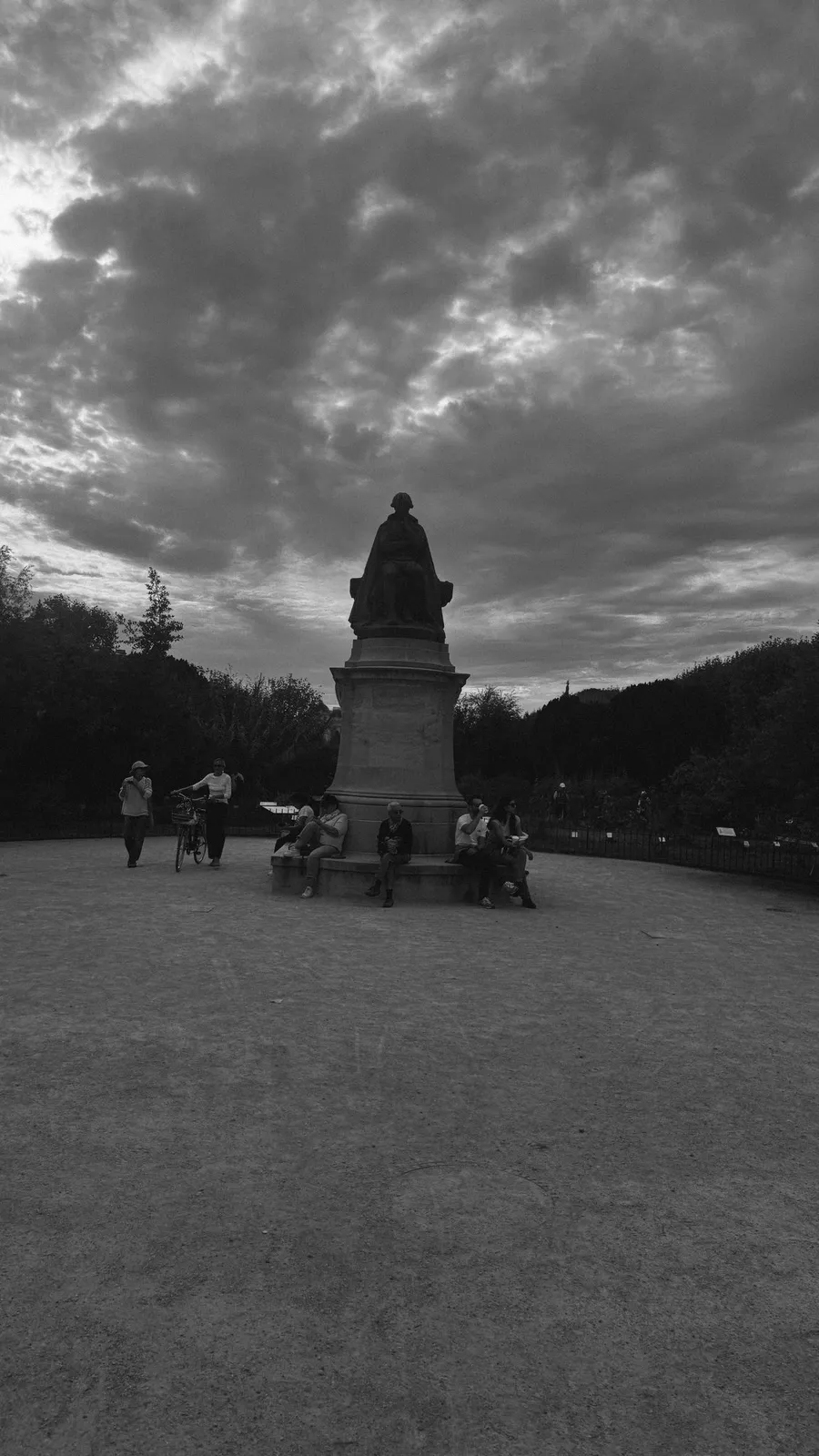 Statue silhouetted under heavy grey clouds in a square