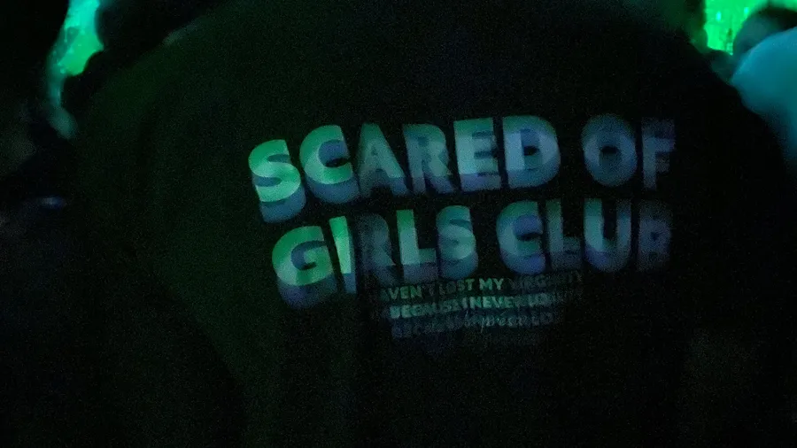 Back of a shirt 'Scared of Girls Club' in green club light