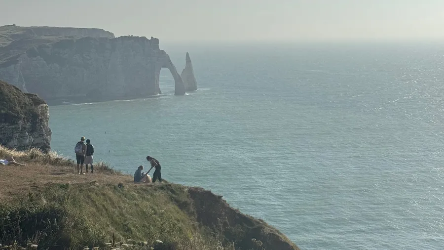 Tiny walkers at the cliff edge against the arch and pale sea