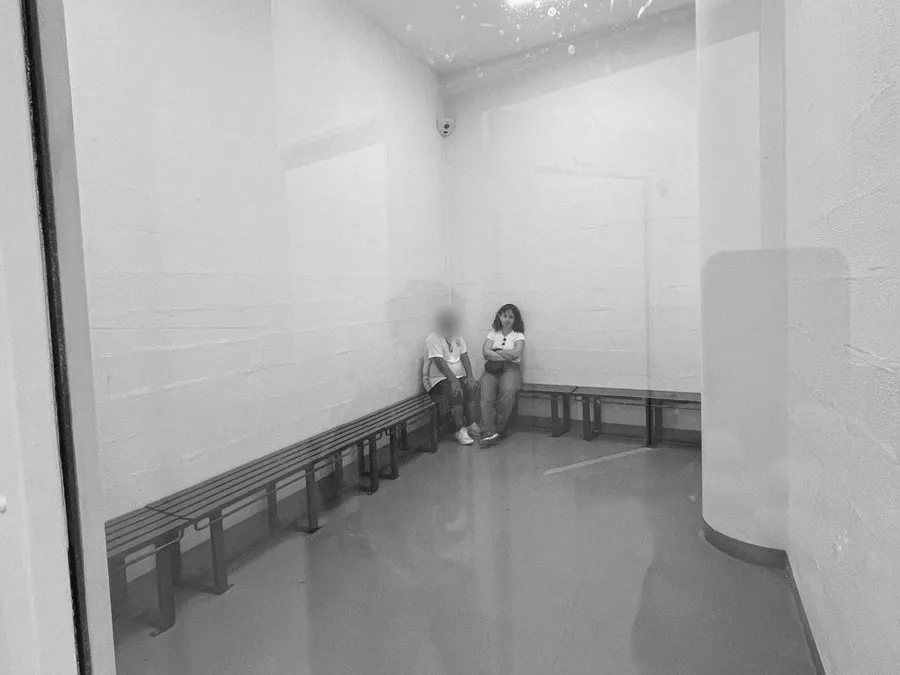 Two people waiting in a bare white holding room, blue benches