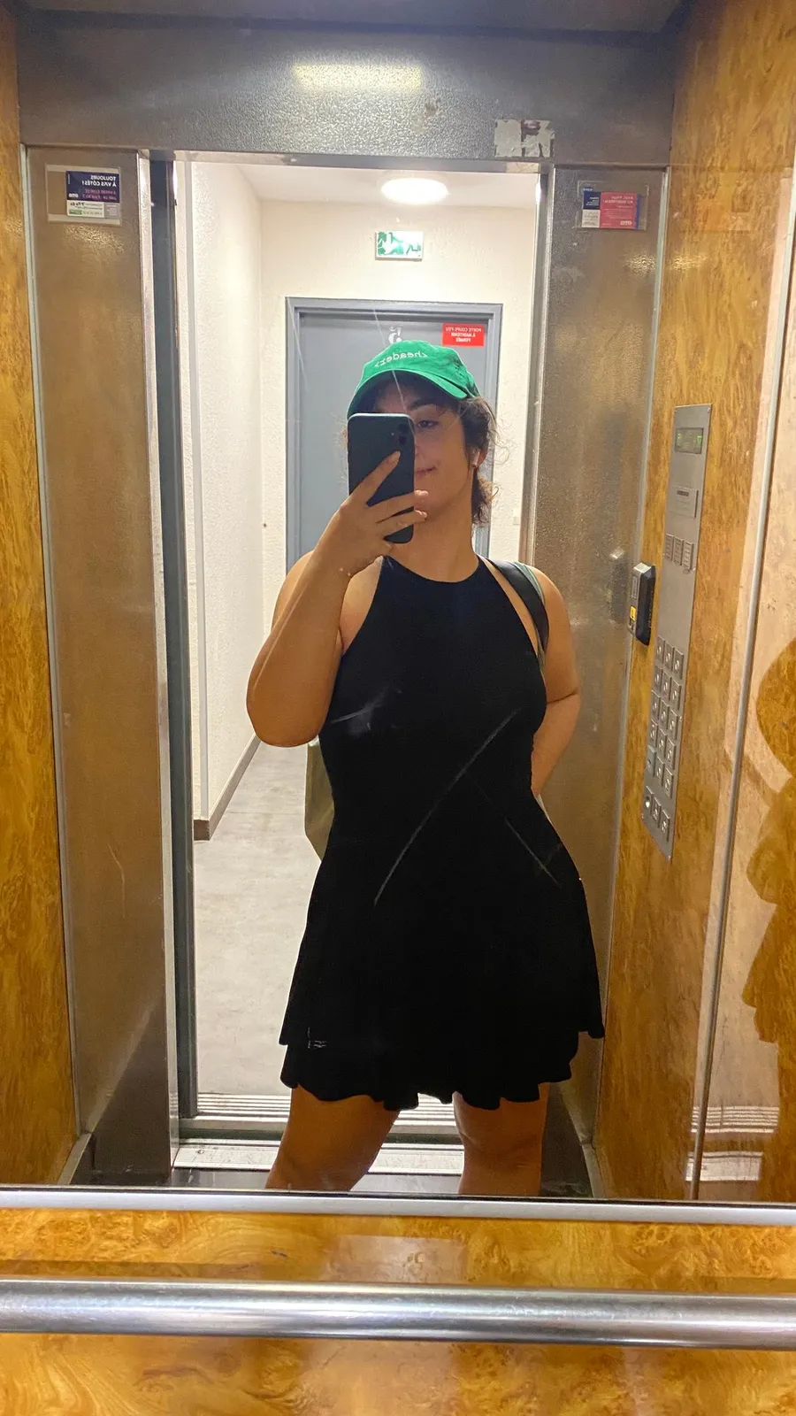 Lift mirror selfie, black dress, green cap