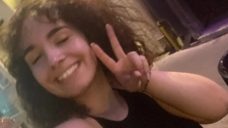 Joyful eyes-closed night selfie, peace sign, wild curls