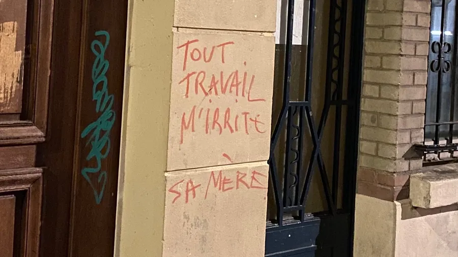 'Tout travail mérite sa mère' scrawled in red on a wall