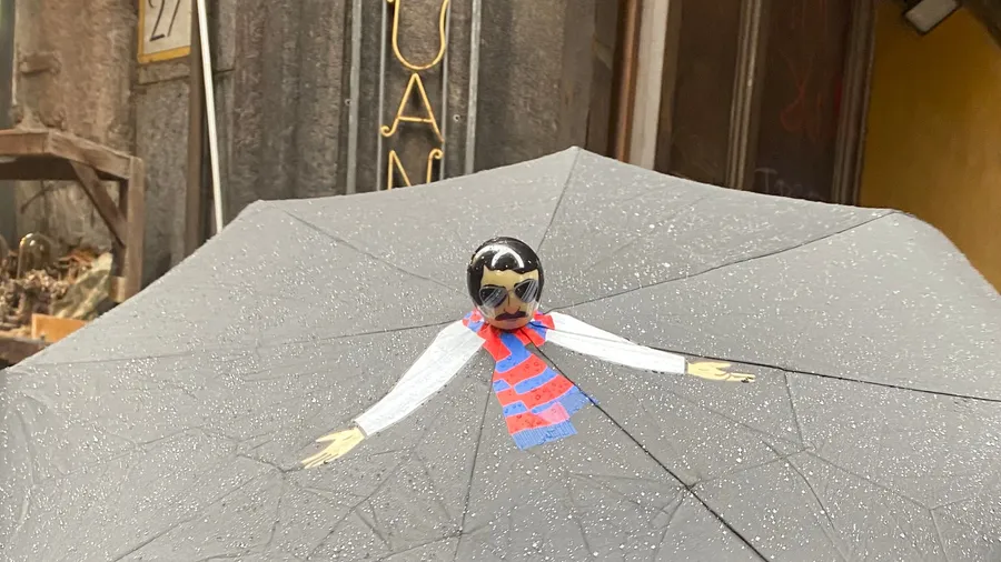 Little figurine man with scarf spread across a wet umbrella