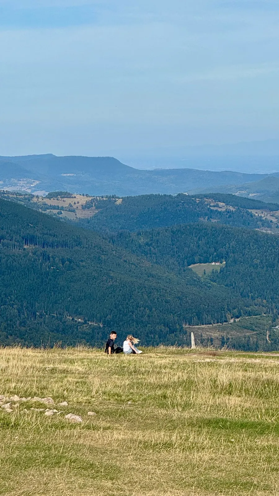 Two tiny figures on the grass before layered blue hills