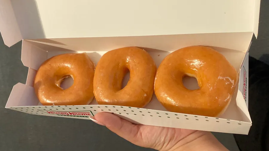 Three glazed doughnuts in an open box, held out