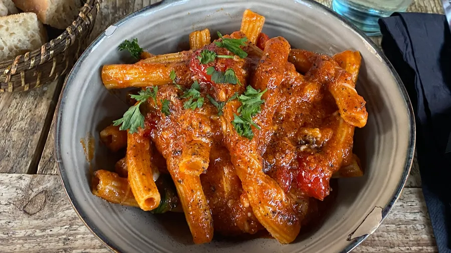Bowl of tomato rigatoni with parsley on a rustic table