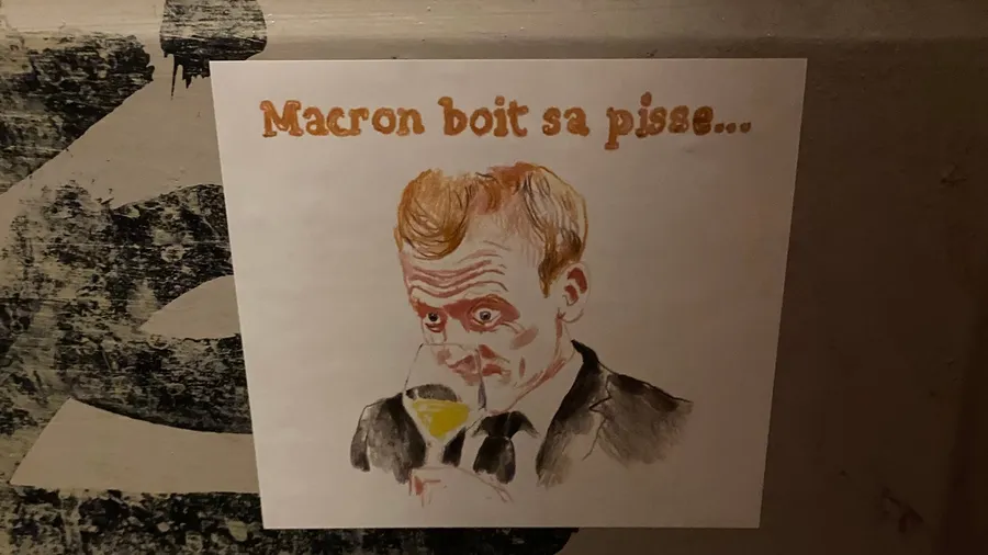 Drawing 'Macron boit sa pisse...' taped on a wall