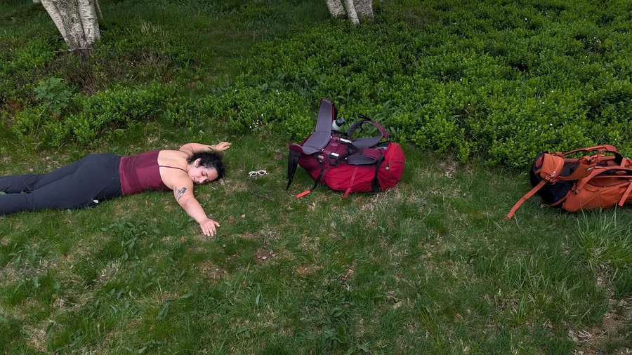 Someone collapsed on the grass beside two backpacks, hike over