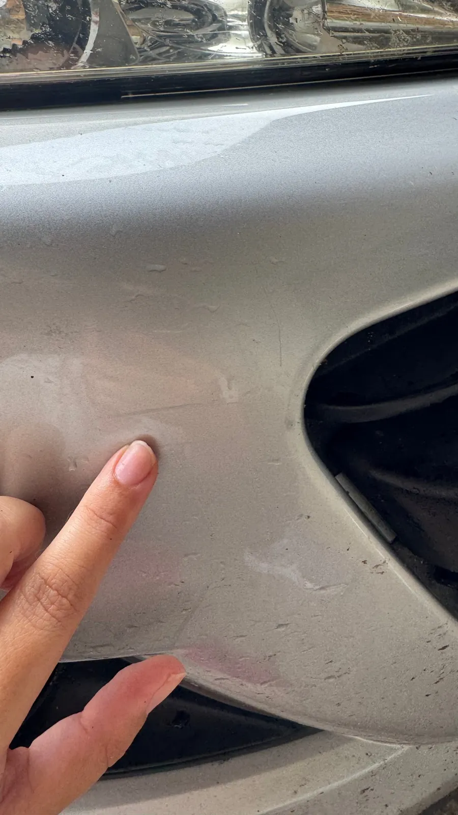 Finger pointing at a dent in a grey car
