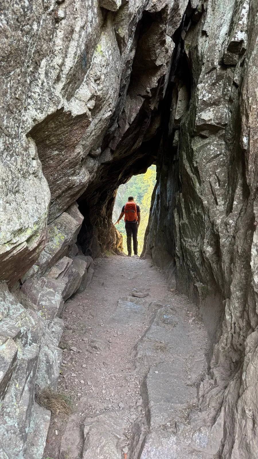 Hiker framed in a narrow rock tunnel opening