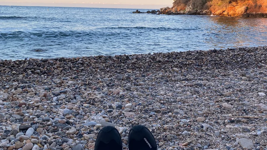 Dawn pebble beach, black shoes at the bottom edge, golden cliff