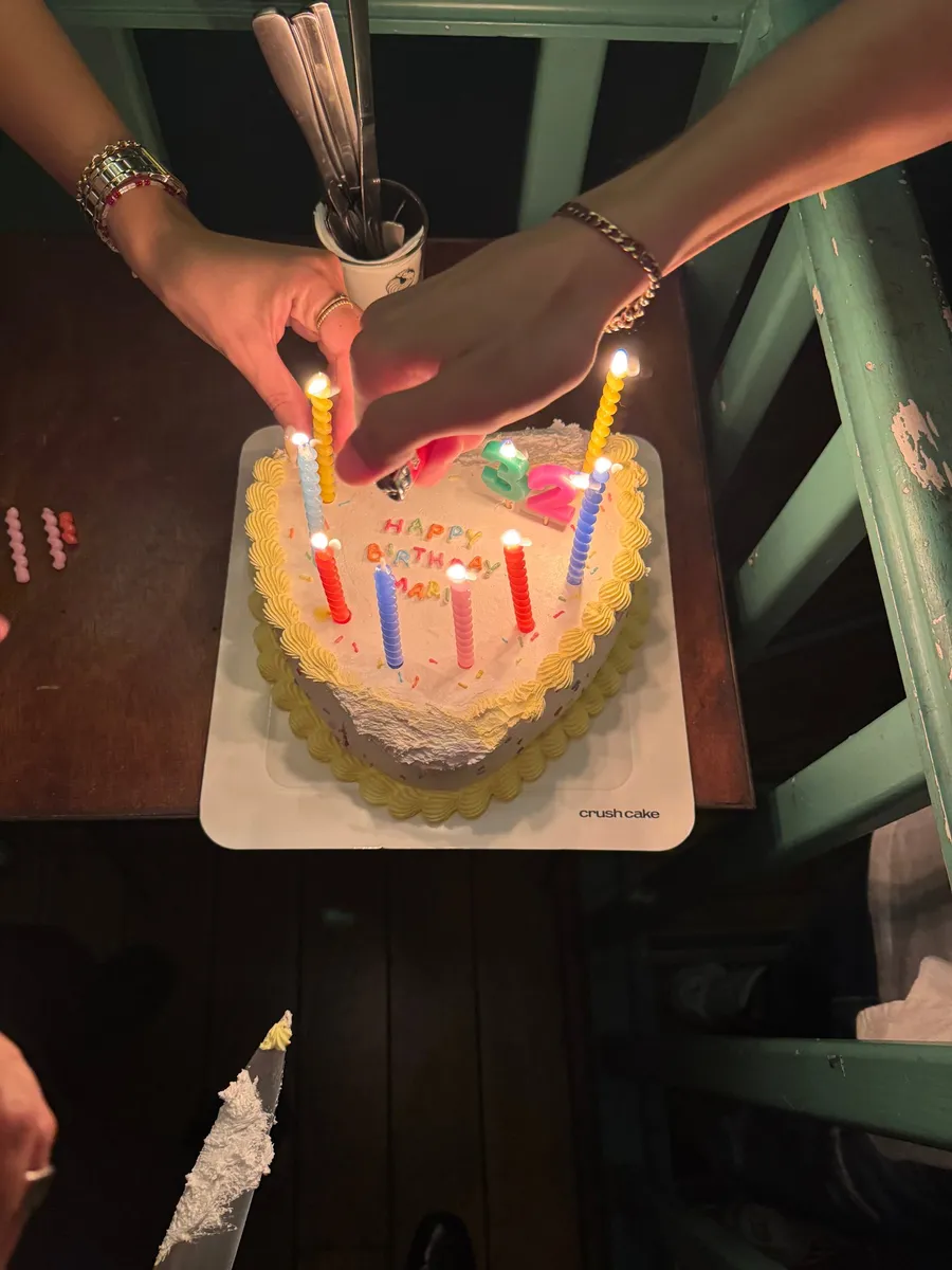 Hands lighting candles on a heart-shaped birthday cake