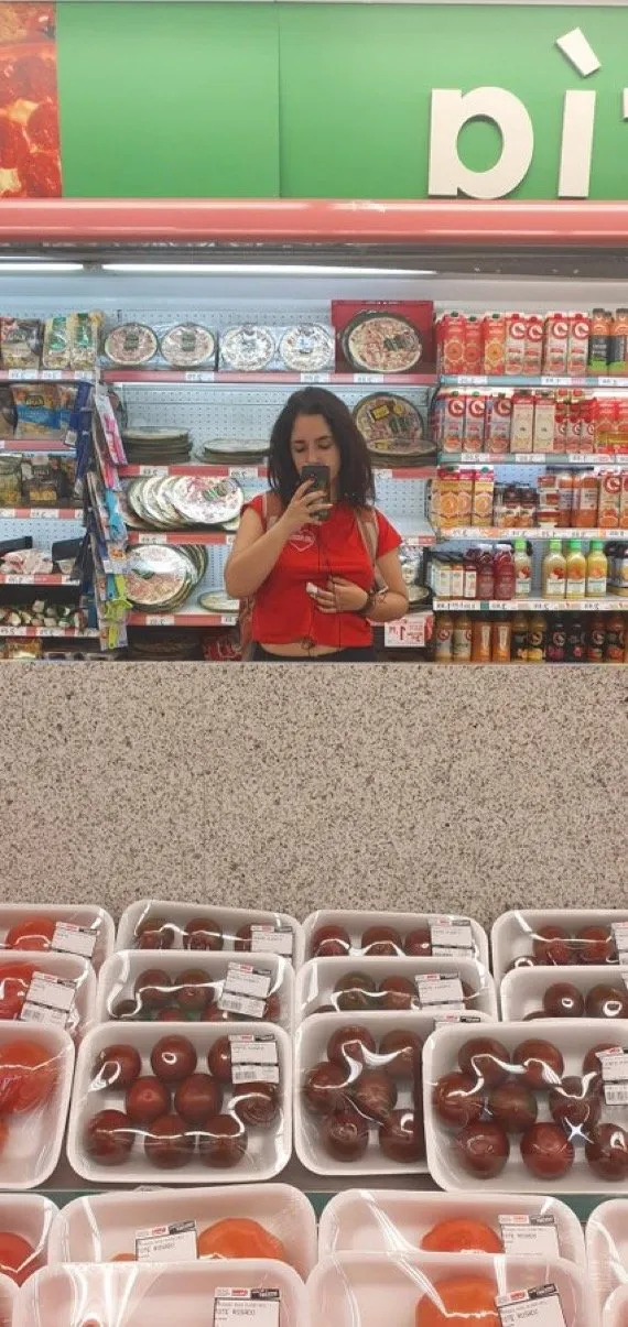 Supermarket mirror selfie above rows of packed tomatoes