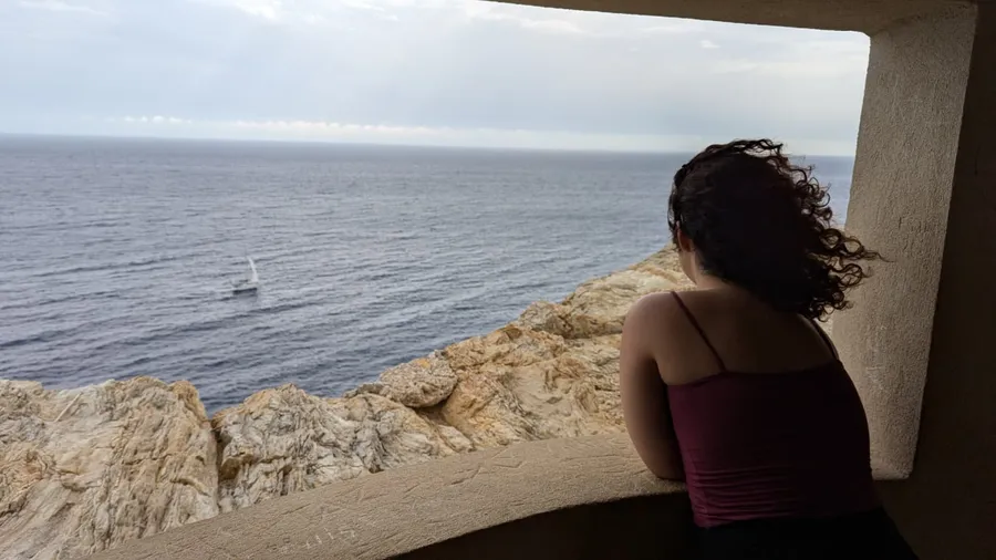 Curls blowing in the wind, looking out to sea through a stone window