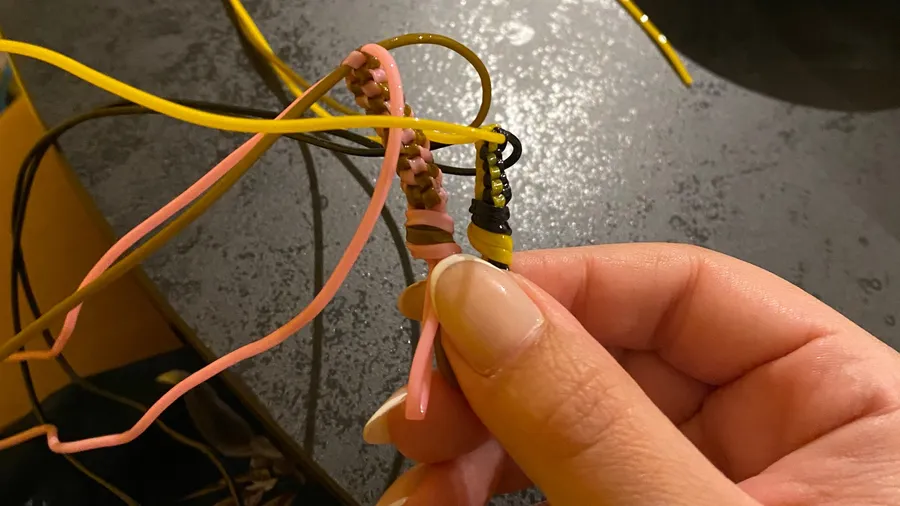 Fingers threading pink and yellow cords into a friendship bracelet