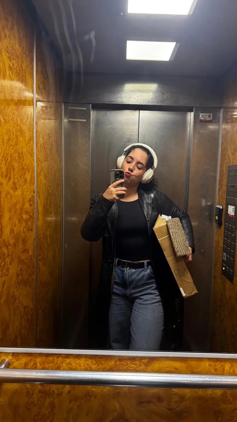 Wood-panelled lift mirror selfie with headphones and parcel
