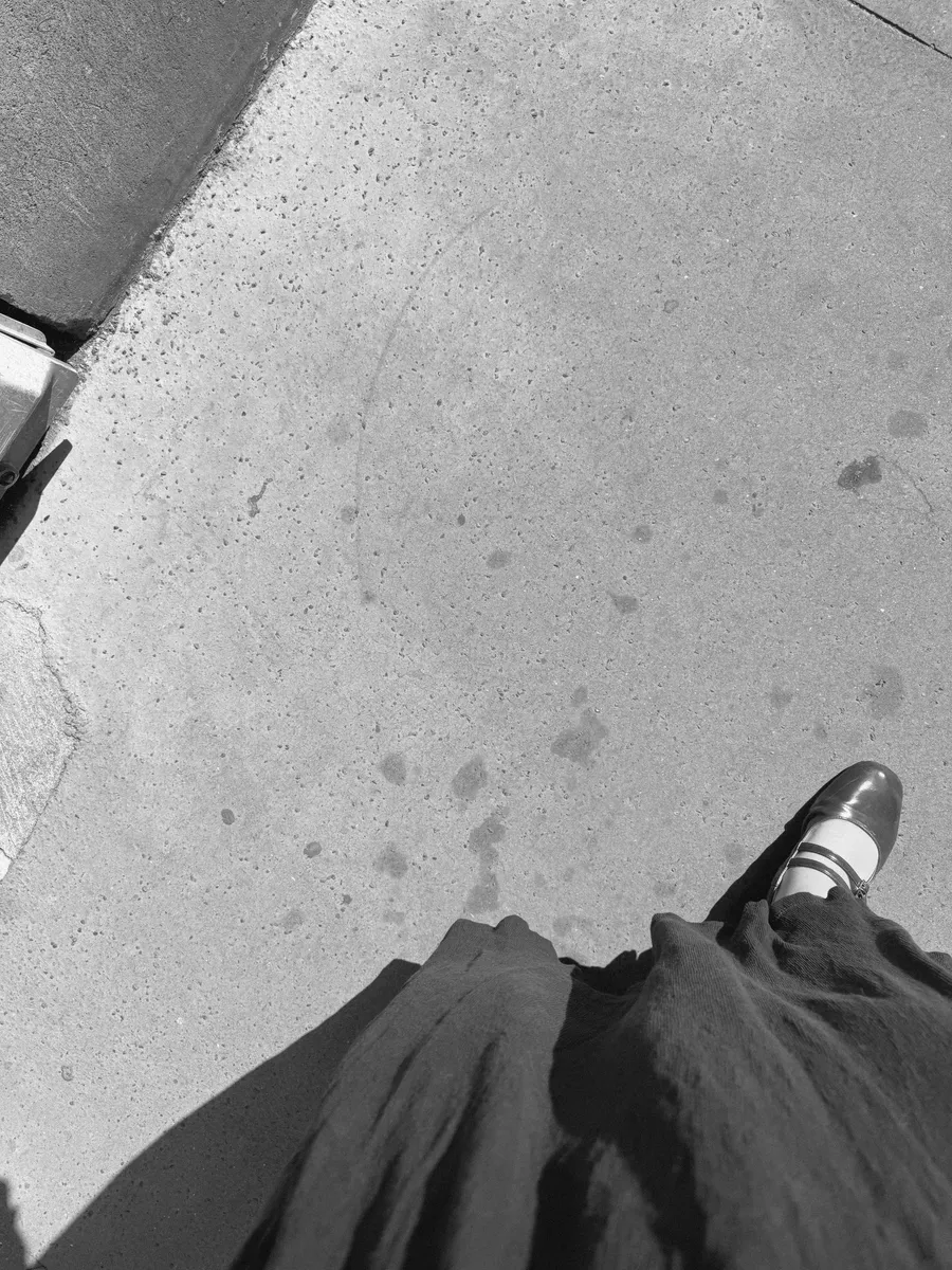 Looking down: one loafer, dark skirt, grey pavement