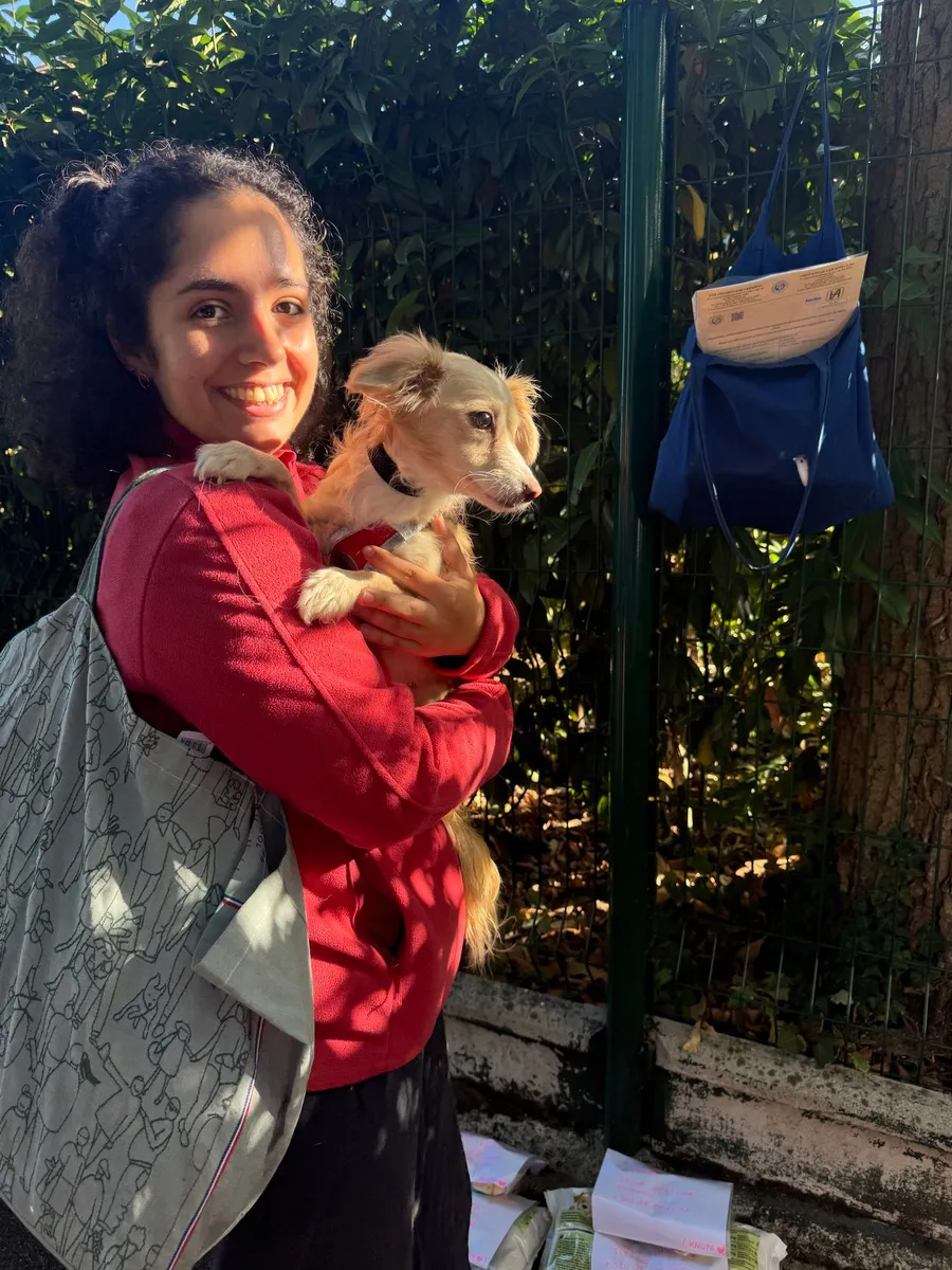 Hugging a small dog on the street, bags on a railing