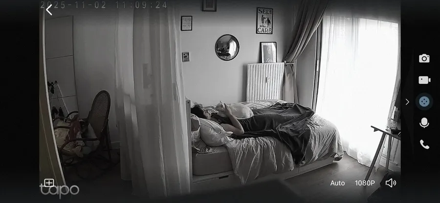 Home camera screenshot: someone asleep in bed, watched