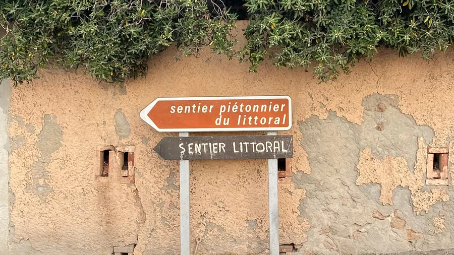 'Sentier du littoral' signs on a peeling ochre wall