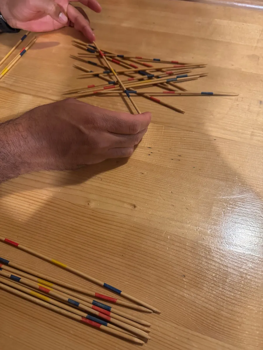 Hands playing mikado, sticks scattered on a glossy table