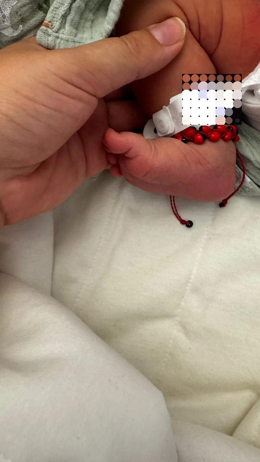 Newborn foot with hospital bracelet and red beads in a hand